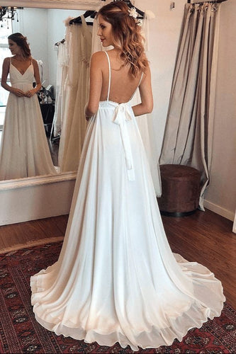 Woman wearing a white wedding dress with a long train in a room with curtains and a mirror.