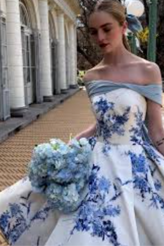 Woman in a floral off-shoulder dress holding a bouquet outdoors.