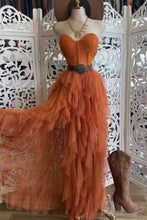 Cargar imagen en el visor de la galería, Mannequin wearing an orange ruffled dress with a belt and brown boots against a decorative white screen.