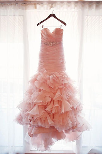 Pink ruffled dress hanging on a hanger against a white curtain.