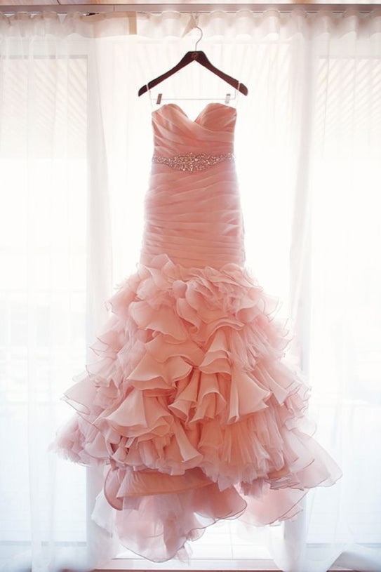 Pink ruffled dress hanging on a hanger against a white curtain.