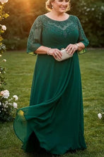 Load image into Gallery viewer, Woman in a green dress standing in a garden with floral decorations at sunset.