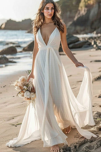 Woman in a white dress standing on a beach with a bouquet of flowers.
