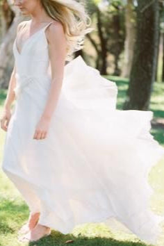 Woman in a white dress standing on grass with trees in the background