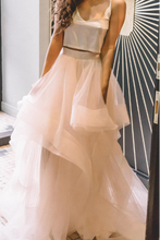 Load image into Gallery viewer, Woman in a white dress standing in front of a decorative wall.