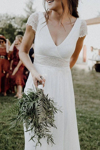 Woman in a white lace dress holding a bouquet of ferns outdoors.