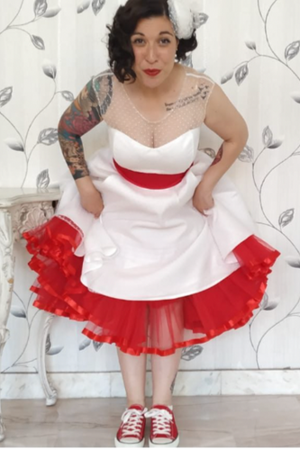 Person wearing a white dress with red accents and red sneakers against a decorative wall.