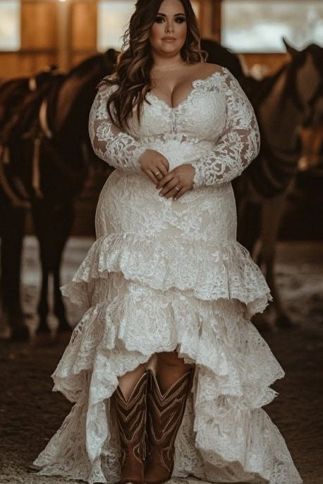 Woman in a lace wedding dress with cowboy boots standing in a barn with horses.