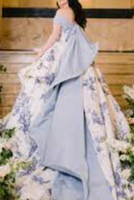 Charger l&#39;image dans la galerie, Woman in a light blue floral dress standing on a decorated staircase with flowers.