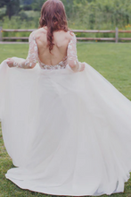 Laden Sie das Bild in den Galerie-Viewer, Woman in a white wedding dress with long sleeves and an open back, standing on grass.