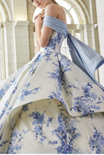 Charger l&#39;image dans la galerie, Woman in a blue and white floral gown with a flowing train in an elegant interior setting.