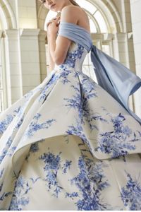 Woman in a blue and white floral gown with a flowing train in an elegant interior setting.